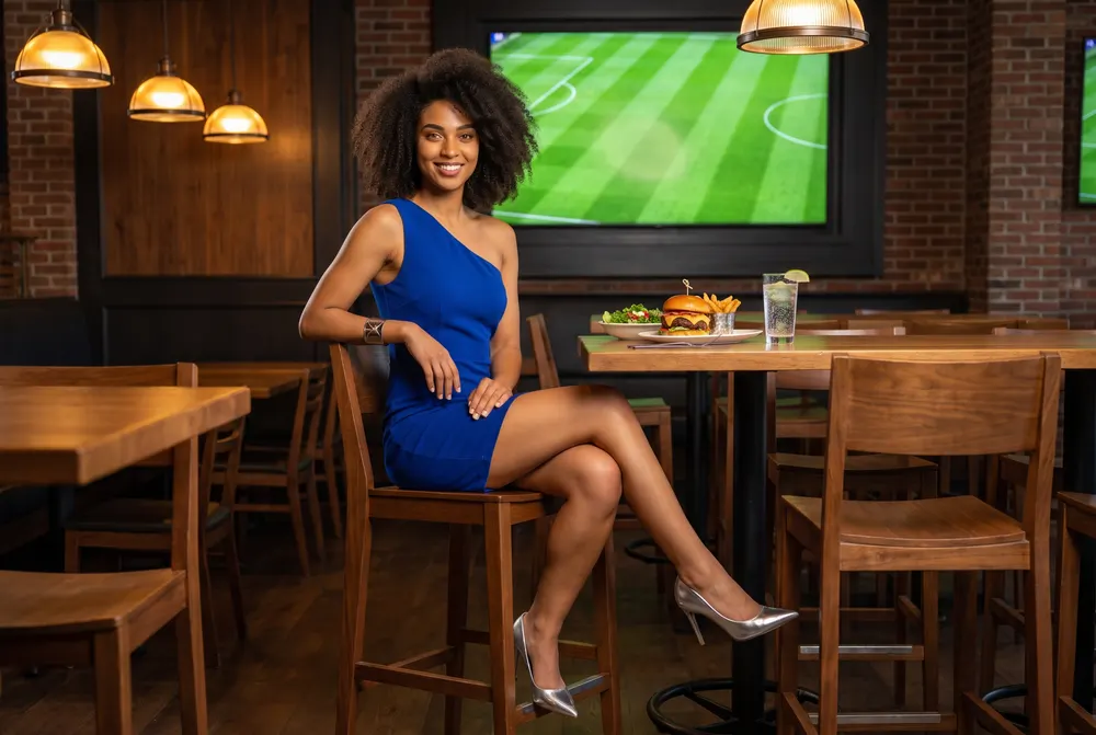 Character created for this guide: a young woman in a royal-blue dress at a high table in a sports pub, with a burger and a glass of sparkling water